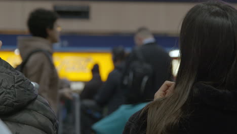 Woman-puts-on-earphones-in-train-station-with-people-passing