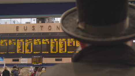 Man-wearing-hat-looking-at-Euston-Station-departure-board