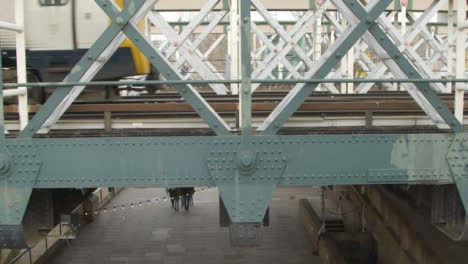 Pedestrians-Walking-Under-Bridge-As-Train-Passes-Above