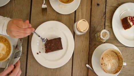Overhead-Pan-Of-Hands-Lifting-Coffee-Mugs-And-Cake-Off-Cafe-Table
