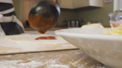 Close-Up-Male-Pouring-Tomato-Sauce-on-Pizza-Dough