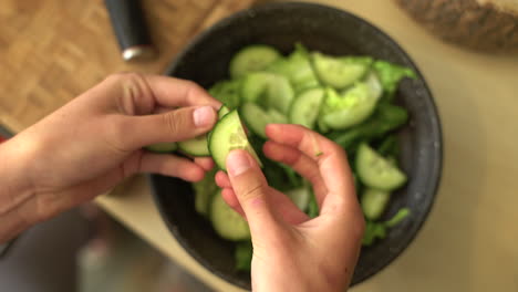 Close-Up-of-Female-Hands-Adding-Sliced-Cucumber-to-Bowl-of-Lettuce