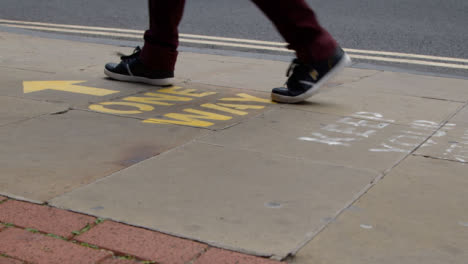 Close-Up-Shot-of-Pedestrians-Feet-Walking-Over-One-Way-Pavement-Marking-In-Oxford