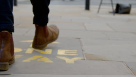 Tracking-Shot-of-Feet-Walking-Over-One-Way-Floor-Marking-In-Oxford-England