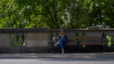 Defocused-Shot-of-People-and-Traffic-Moving-In-Front-of-Woman-Sat-On-Bench-01