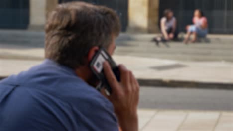 Defocused-Shot-of-Man-Talking-On-Teléfono-Whilst-Sitting-On-Street-In-Oxford-02