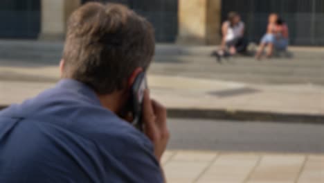 Defocused-Shot-of-Man-Talking-On-His-Phone-Whilst-Sitting-On-Street-In-Oxford-01