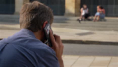 Defocused-Shot-of-Man-Talking-On-His-Phone-Whilst-Sitting-On-Street-In-Oxford-02