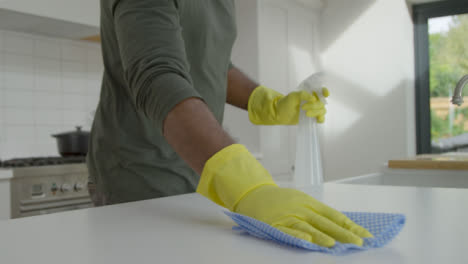 Hombre-Limpiando-La-Superficie-De-Trabajo-De-La-Cocina-Con-Guantes-De-Goma-Y-Spray-Desinfectante