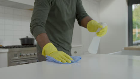 Hombre-Limpiando-La-Superficie-De-Trabajo-De-La-Cocina-Con-Guantes-De-Goma-Y-Desinfectante