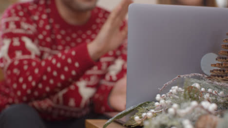 Extreme-Close-Up-of-Christmas-Table-Decorations-In-Front-of-Couple-Using-Laptop-