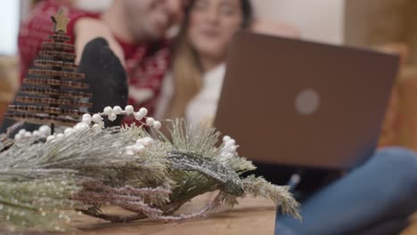 Extreme-Close-Up-of-Christmas-Decorations-As-Couple-In-Background-Interact-with-Laptop