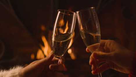 Close-Up-of-Two-People-Bringing-Their-Champagne-Glasses-Together-In-Front-of-Burning-Fire-