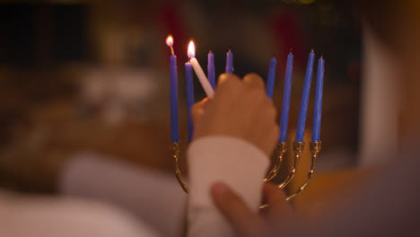 Over-the-Shoulder-Shot-of-Couple-Lighting-Candles-of-Menorah-During-Hanukkah