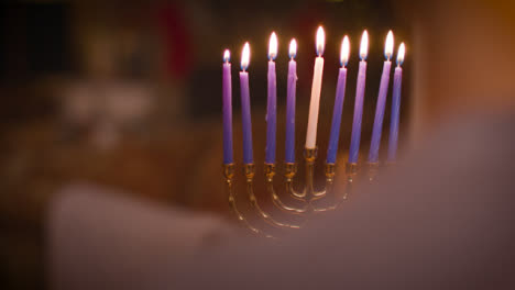 Over-the-Shoulder-Shot-of-Young-Couple-Looking-at-Lit-Menorah-During-Hanukkah