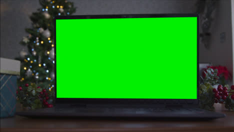 Close-Up-Shot-of-a-Laptop-Green-Screen-On-Table-In-Front-of-Christmas-Themed-Background