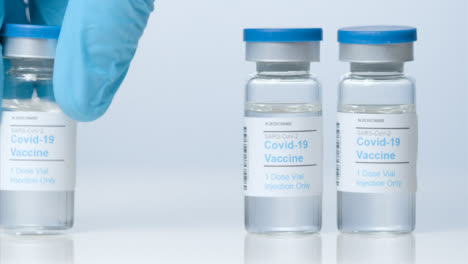 Sliding-Close-Up-Shot-of-Three-Vials-of-Covid-Vaccine-as-Hand-Takes-One-Away