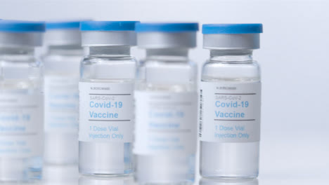 Sliding-Extreme-Close-Up-Shot-Past-Vials-of-Coronavirus-Vaccine-As-Hand-Uses-Syringe