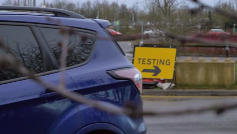 Handheld-Pull-Focus-Shot-of-Cars-Driving-Past-COVID-Test-Site-Road-Sign