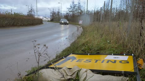Wide-Shot-of-Car-Driving-Past-Fallen-Over-COVID-19-Test-Site-Road-Sign