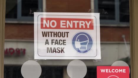 Handheld-Close-Up-Shot-of-COVID-19-Face-Mask-Sign-In-Shop-Window