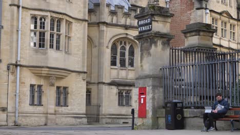Wide-Shot-of-Student-Sitting-On-Bench-On-Corner-of-Broad-Street-In-Oxford
