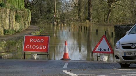 Long-Shot-of-Car-Driving-Past-Road-Closed-and-Flood-Signs-In-Front-on-Flooded-Road