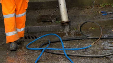 Handheld-Shot-of-Drainage-Workers-Feet-as-They-Retract-Pipe-Use-to-Clean-Blocked-Drain