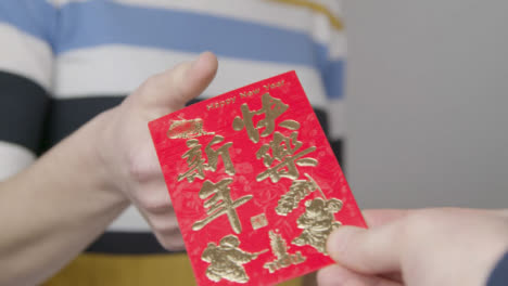 Close-Up-Shot-of-Hand-Giving-Chinese-New-Year-Red-Envelope-to-Person