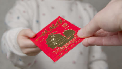 Close-Up-Shot-of-Hand-Giving-Chinese-New-Year-Red-Envelope-to-Niño