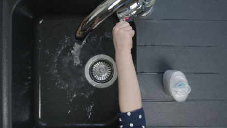 Top-Down-Shot-of-Young-Childs-Hands-Turning-On-Kitchen-Tap
