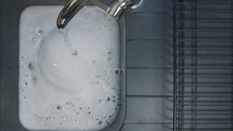 Top-Down-Shot-of-Male-Hand-Turning-Off-Running-Tap-as-Sink-Fills-with-Soapy-Water