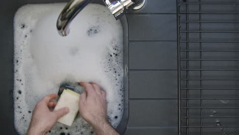 Top-Down-Shot-of-Male-Hands-Washing-Cup-In-Sink-of-Soapy-Water