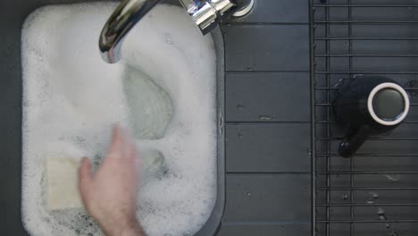Top-Down-Shot-of-Male-Hands-Placing-Dirty-Dishes-into-Sink-of-Soapy-Water