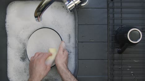 Top-Down-Shot-of-Male-Hands-Washing-Plate-In-Sink-of-Soapy-Water