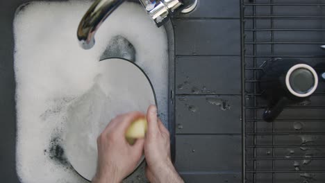 Top-Down-Shot-of-Male-Hands-Washing-Plate-In-a-Sink-of-Soapy-Water