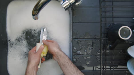 Top-Down-Shot-of-Male-Hands-Washing-Knives-In-Sink-of-Soapy-Water