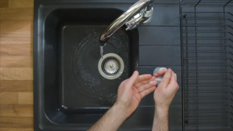 Top-Down-Shot-of-Male-Hands-Turning-On-Kitchen-Tap-and-Washing-with-Soap