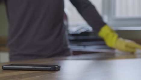 Sliding-Close-Up-Shot-of-Phone-On-Kitchen-Surface-As-Adult-Cleans-In-Background