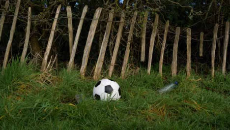 Medium-Shot-of-Soccer-Ball-Landing-In-Front-of-Dilapidated-Fence-Next-to-Litter
