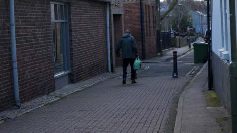 Handheld-Wide-Shot-of-Elderly-Man-Walking-Down-Alleyway-