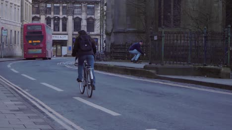 Handheld-Shot-of-Cyclist-Riding-Up-Road-Past-Skater-