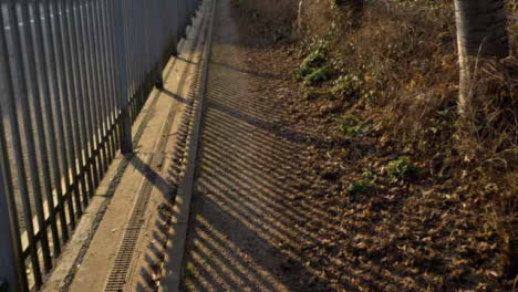 Tracking-Shot-Along-Footpath-Next-to-Metal-Fence