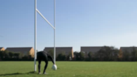 Defocused-Wide-Shot-of-Rugby-Player-Picking-Ball-and-Tee-Up-from-Next-to-Post
