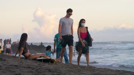 Medium-Shot-of-Young-Woman-Sitting-On-Beach-as-People-Walk-Past