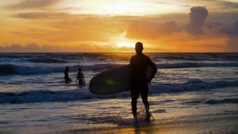 Handheld-Medium-Aufnahme-Eines-Surfers,-Der-Entlang-Des-Echostrandes-Läuft,-Der-Sich-Gegen-Sonnenuntergang-Abhebt