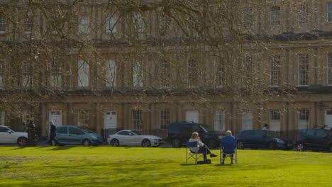 Wide-Shot-of-Senior-Couple-Sitting-On-Grass-Outside-Crescent-Housing
