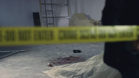 Sliding-Wide-Shot-of-Crime-Scene-In-Warehouse-with-Crime-Scene-Tape-Being-Pulled-In-Foreground