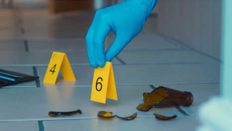 Sliding-Long-Shot-of-Forensic-Placing-Evidence-Tag-On-Floor-at-Crime-Scene