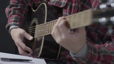 Medium-Shot-of-Musician-Playing-Guitar-and-Writing-In-Notepad